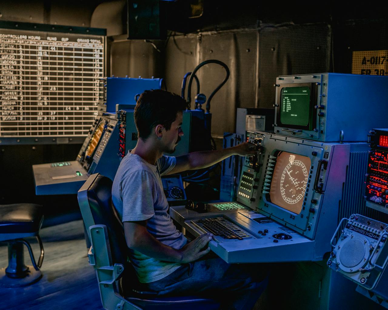 services-02 A man working at control panels in a dimly lit industrial room with various monitors.